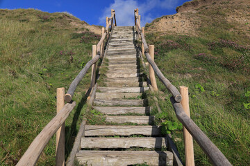 Photo with a view of a wooden stairs with a railing leading up from the beach on the North Sea coast near Bovbjerg Lighthouse in Denmark