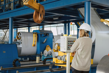 Industrial equipment for working with coil metal. Decoiler holds and unwinds metal coil. Slitting or cut-to-length line - cut coil metal into strips. Woman wearing helmet is working there.