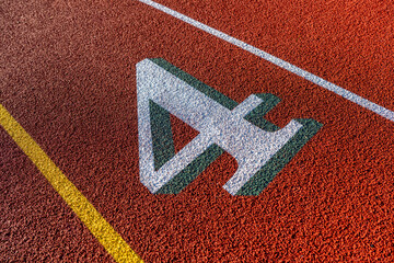 Close up photo of outdoor running track lane white number four, 4, with green shadow, on a new red track with white lane lines.