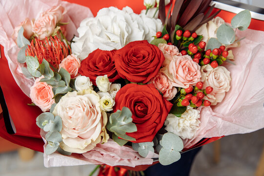 Luxurious bouquet featuring classic red and pale pink roses, white hydrangea, eucalyptus leaves, and vibrant red hypericum berries, wrapped in red paper