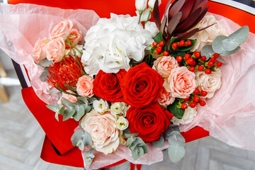 Luxurious mixed bouquet of red and pale blush pink roses, white hydrangea, red hypericum berries, and a red protea, wrapped in red and pink paper