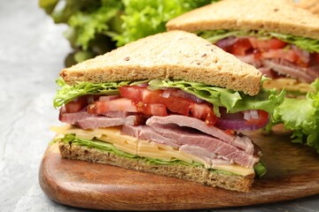 Delicious sandwiches with ham, cheese and vegetables on grey textured table, closeup