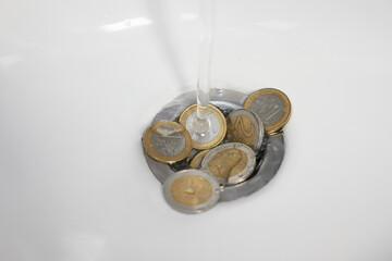 Coins and water going down sink drain, closeup