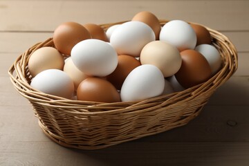 Many raw chicken eggs in wicker basket on wooden table, closeup