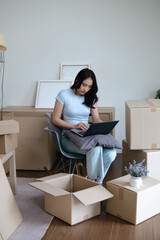 Female Asian using laptop amid relocation boxes preparing for move