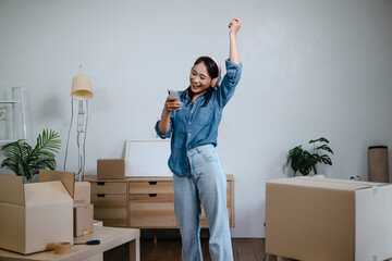 Asian woman using mobile phone among moving boxes for home relocation