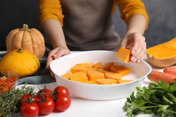 Woman putting pumpkin into baking dish at white wooden table, closeup