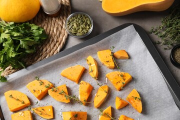 Pieces of fresh pumpkin with thyme and other spices on grey table, flat lay