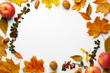 Frame of dry autumn leaves, cotoneaster branches with red berries, apples and nuts on white background, flat lay. Space for text