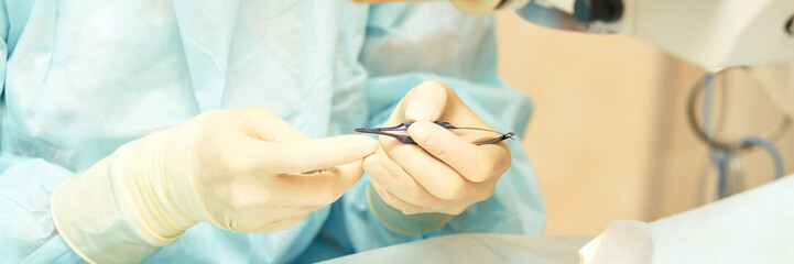 Close-up of surgeon performing delicate surgery wearing blue scrubs and gloves in operating room.