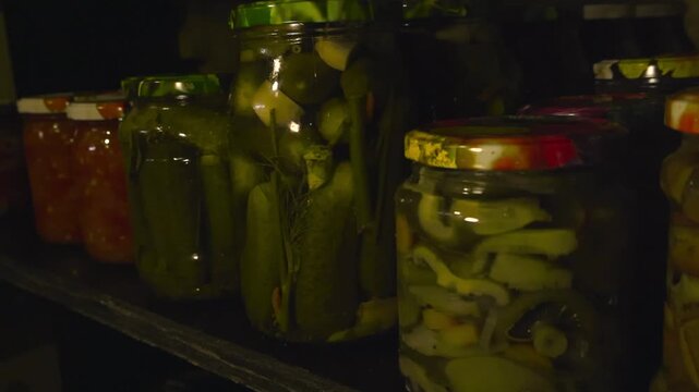 Close up view of jars of preserves or pickles on a cellar shelf in a dark basement. Tomatoes, garlic, cucumbers and chillys are preserved in the liquid. Tasty.