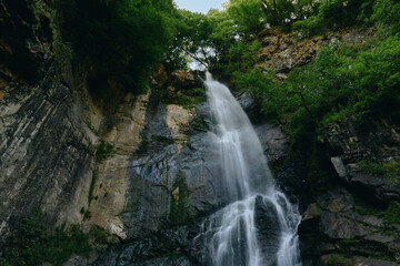 Obraz premium Majestic waterfall cascading down rocky cliffs surrounded by lush green forest, creating a serene and natural landscape full of movement and freshness.
