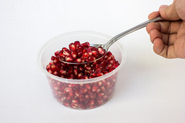 A spoonful of juicy pomegranate red arils from inside a transparent plastic container, isolated on white background.