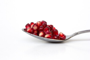 Red pomegranate seeds or arils in the stainless steel spoon, isolated on white background. Pomegranates can be eaten fresh, juiced, or used in cooking, and also used to make juices, jams, and sauces.