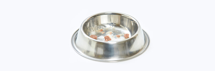 Empty stainless steel pet bowl with food residue on white background.
