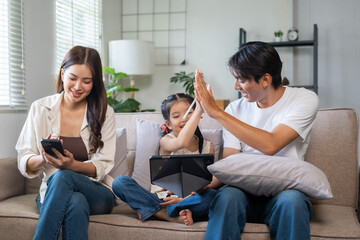Asian family enjoying time together on couch, father and daughter high fiving, mother using mobile phone