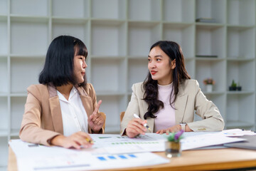 Asian businesswomen collaborating, reviewing charts and graphs during a corporate meeting, contributing ideas, and sharing insights