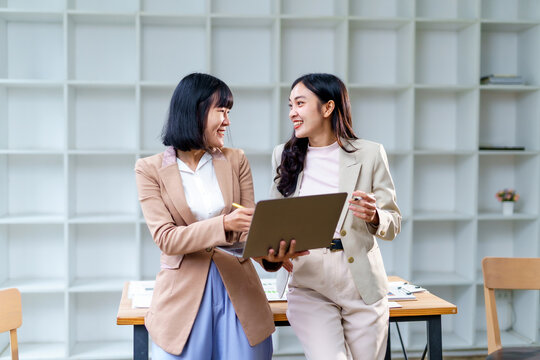 Two smiling businesswomen are collaborating on a laptop, discussing new ideas and working together in a modern office environment