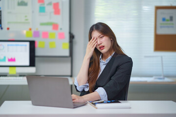Young businesswoman suffering burnout, eyestrain, and tired eyes from working on a laptop computer in the office
