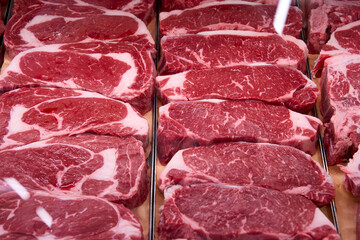 Fresh raw beef steaks displayed in a butcher shop or supermarket counter. Marbled meat ready for sale or cooking, arranged in neat rows.