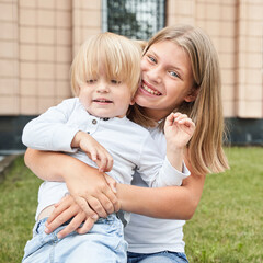 Smiling caucasian female teen hugging caucasian male child outdoors in casual clothing.