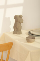 Minimalist still life with abstract torso sculpture, sunlit table setting and neutral ceramic dishes