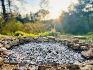 Fire Pit After Burn – Ashes and Logs in Stone Circle at Sunrise or Sunset