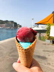 A person holding a cone of ice cream with a pink and blue swirl. cone