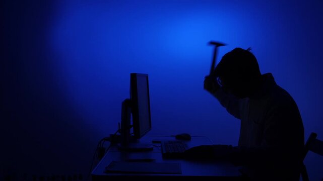 Man in silhouette smashing computer with hammer feeling frustration