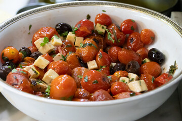 Bowl of Mediterranean salad made with cherry tomatoes, black olives and cubed cheese, the salad has a beautiful shine