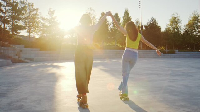 Young women join hands and turn on quad skates in sunset park