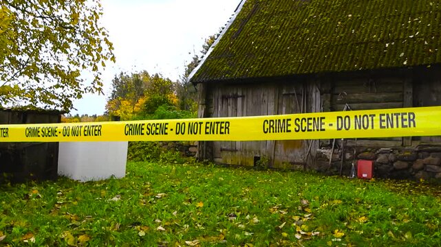 Yellow police line Crime Scene forensic investigation tape ribbon in front of a abandoned and old vintage farm house or shed in countryside with autumn nature and yellow leaves. Moss covering roof.
