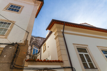 A low-angle view captures the contrasting facades of weathered and pristine white buildings under a clear blue sky