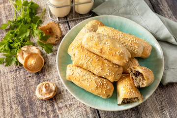 Homemade savory mushroom pastries with sesame seeds on rustic wooden table setting.