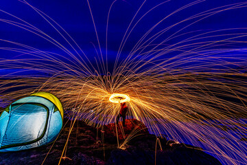 Langzeitbelichtung mit brennender, rotierender Stahlwolle in der Nacht. Funken fliegen kreisförmig...