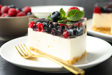 Piece of delicious cheesecake with berries and mint on black wooden table, closeup