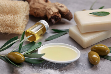 Handmade soap bars, olives, green leaves, oil and loofah on gray textured table, closeup