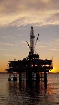 Aerial shot of an offshore oil platform at sunset. Vertical Video.