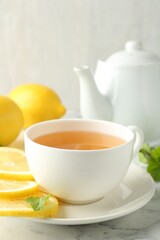 Aromatic tea in cup with lemons and mint on white marble table, closeup