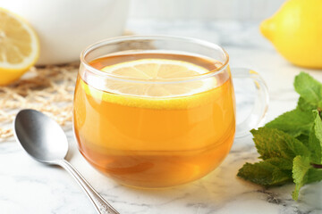 Aromatic tea in cup with lemon, mint and spoon on white marble table, closeup