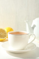 Aromatic tea in cup, lemons and teapot on white table, closeup