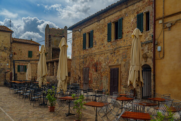 Medieval Tuscan Piazza with Stone Buildings, Empty Cafe Tables and Closed Umbrellas