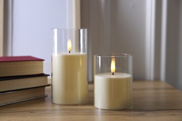 Decorative LED candles and books on wooden table indoors, closeup