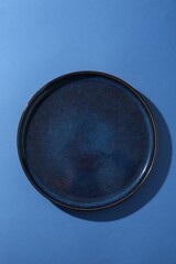 Stylish ceramic plate on blue background, top view