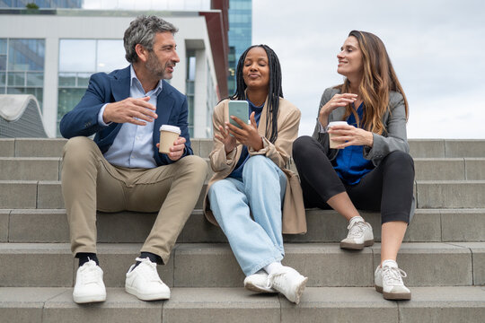Diverse coworkers having coffee break on urban stairs