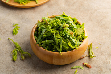Young tamarind leaves for cooking in wooden bowl.