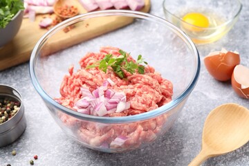 Raw minced meat with onion, parsley, spices and egg on grey table, closeup