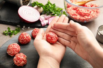 Woman making meatball from ground meat at grey table, closeup
