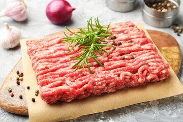 Raw minced meat with rosemary and spices on grey textured table, closeup