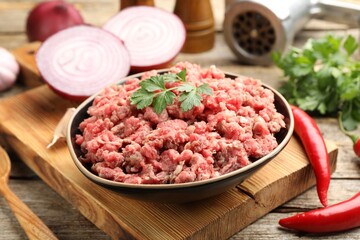 Raw minced meat with parsley, onion and chili peppers on wooden table, closeup